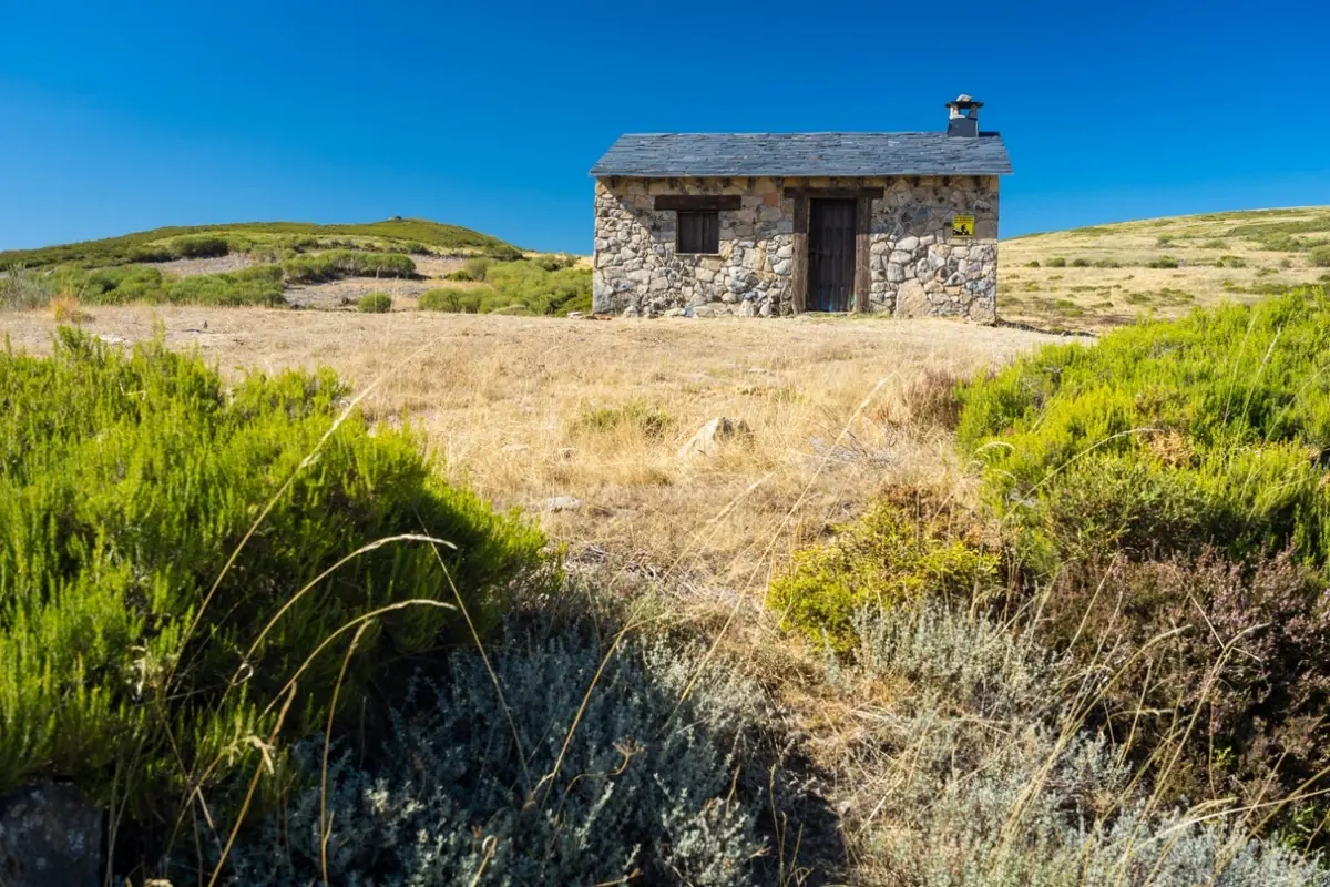Refugio de piedra entre pastos y matorral de montaña