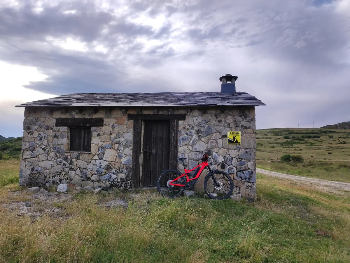 Refugio de piedra con bicicleta apoyada en la fachada bajo un cielo nublado