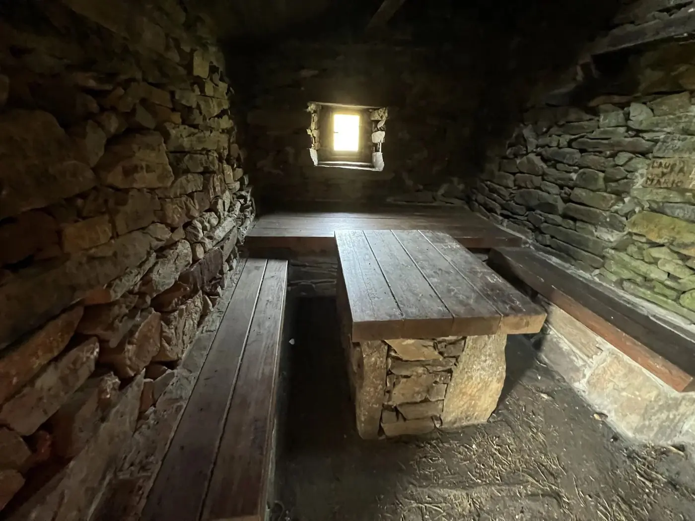 Interior de un refugio de montaña con mesa y banco de piedra y madera