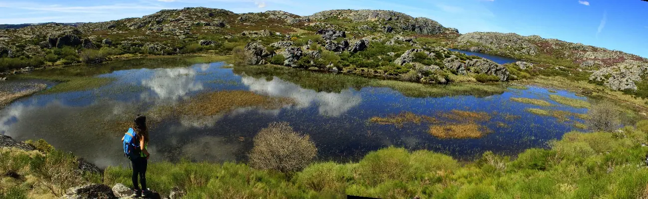 Panorámica de una laguna de montaña con un senderista en la orilla