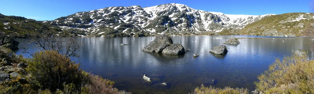Laguna con bloques de granito y cumbres nevadas reflejadas
